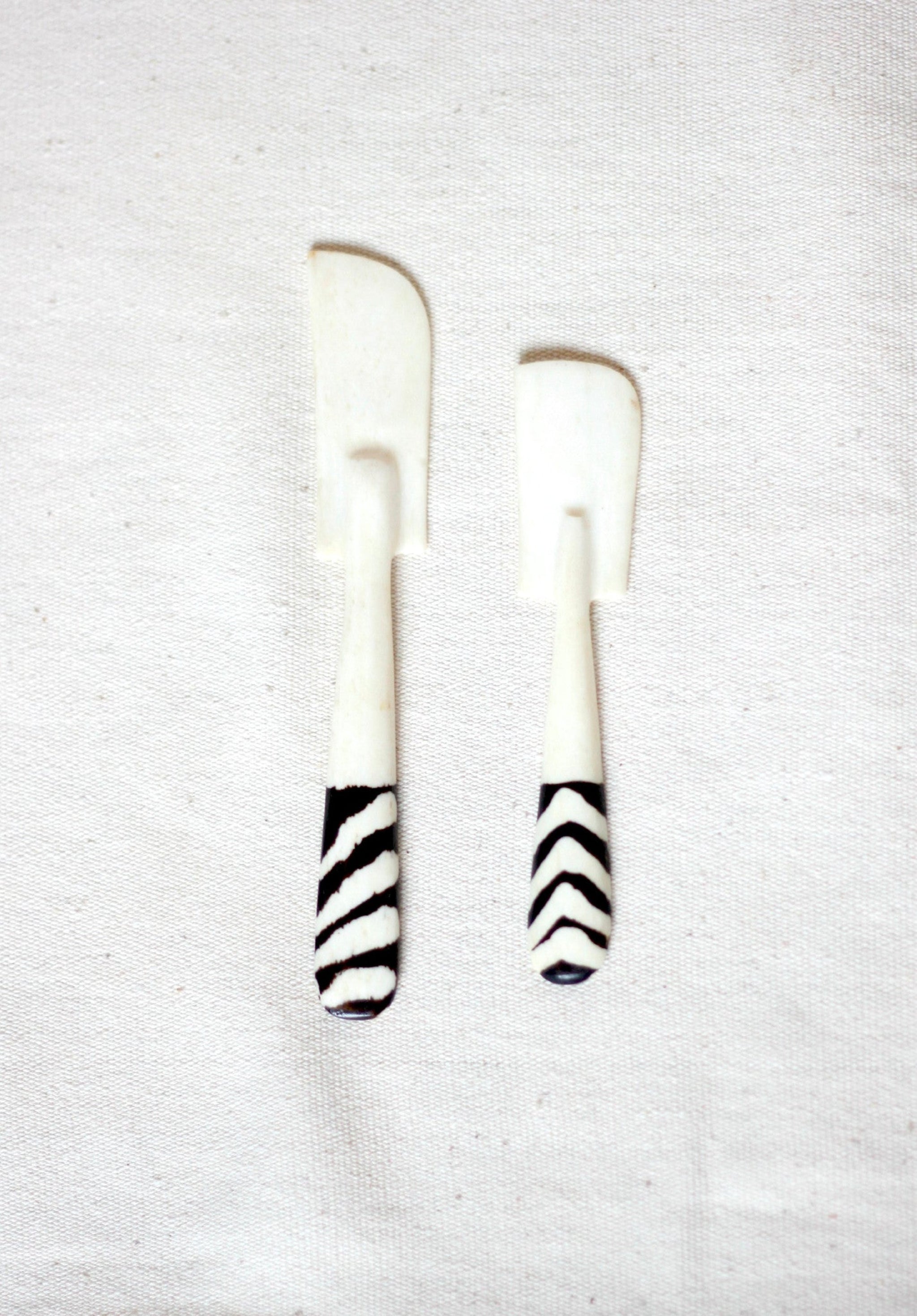 Two white cow horn knives with black and white zebra-patterned handles, displayed on a textured off-white fabric background.