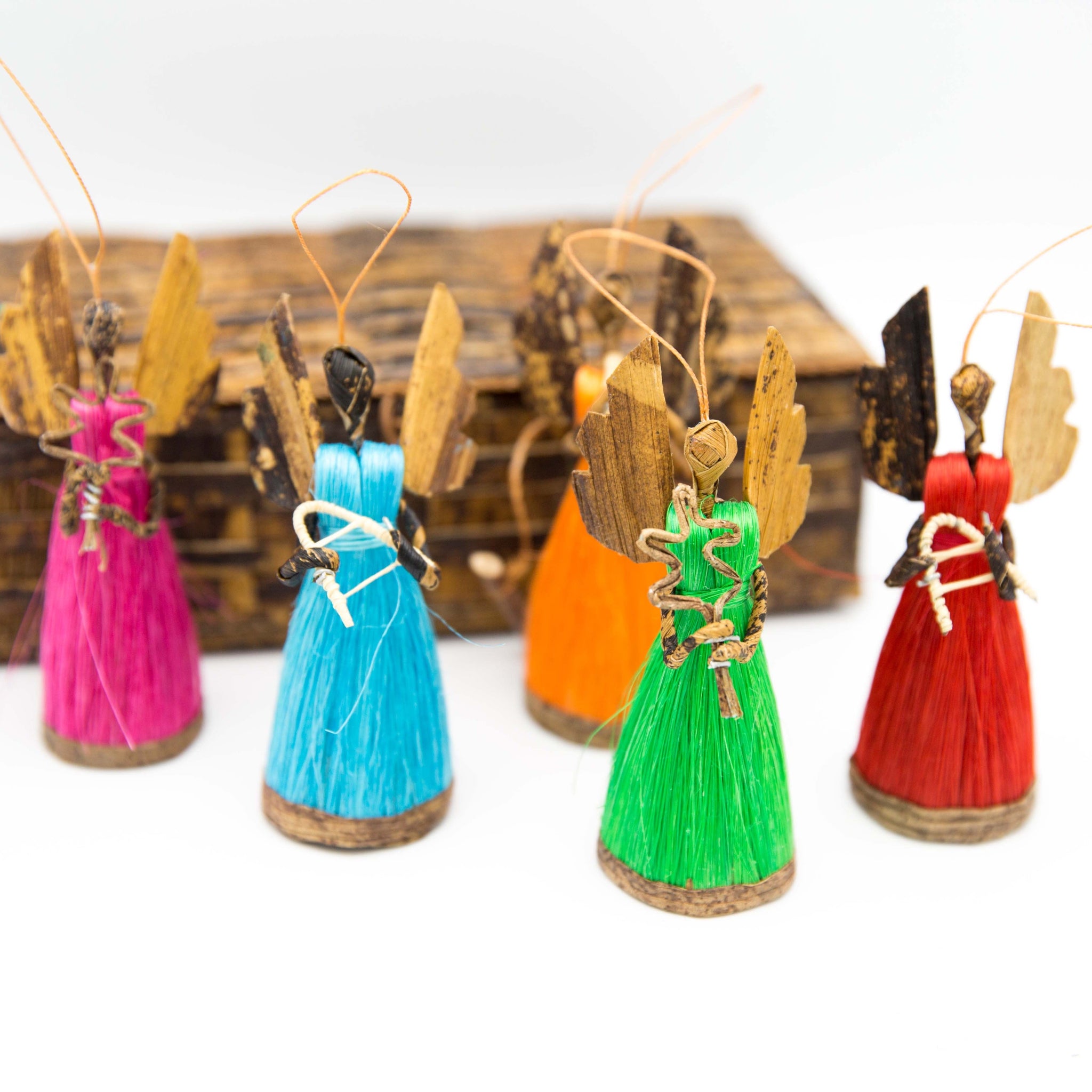A set of five multicolored angel ornaments made from sisal grass fiber and dried banana leaves, each holding a different symbol.