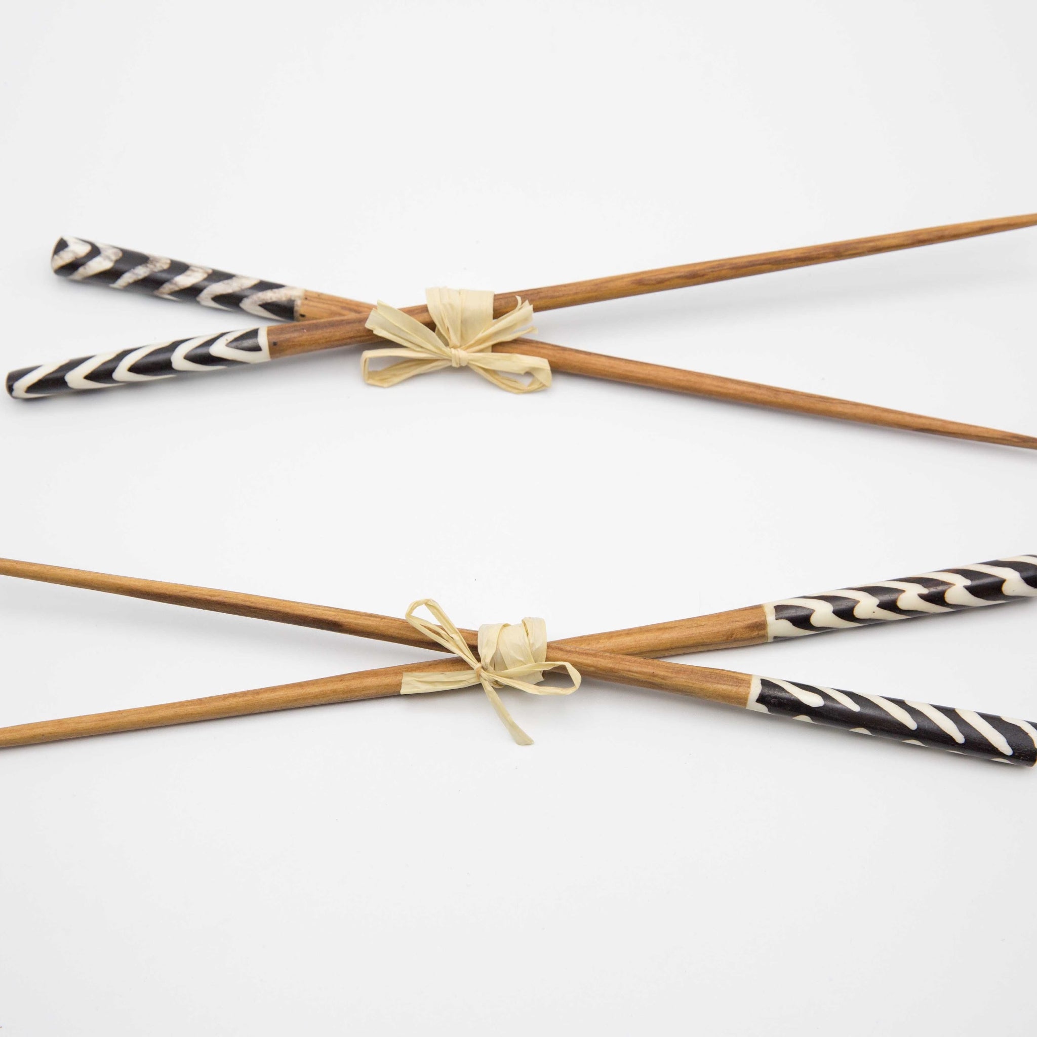 Two pairs of wooden chopsticks with black and white patterned handles, tied with beige ribbon bows, on a white background.