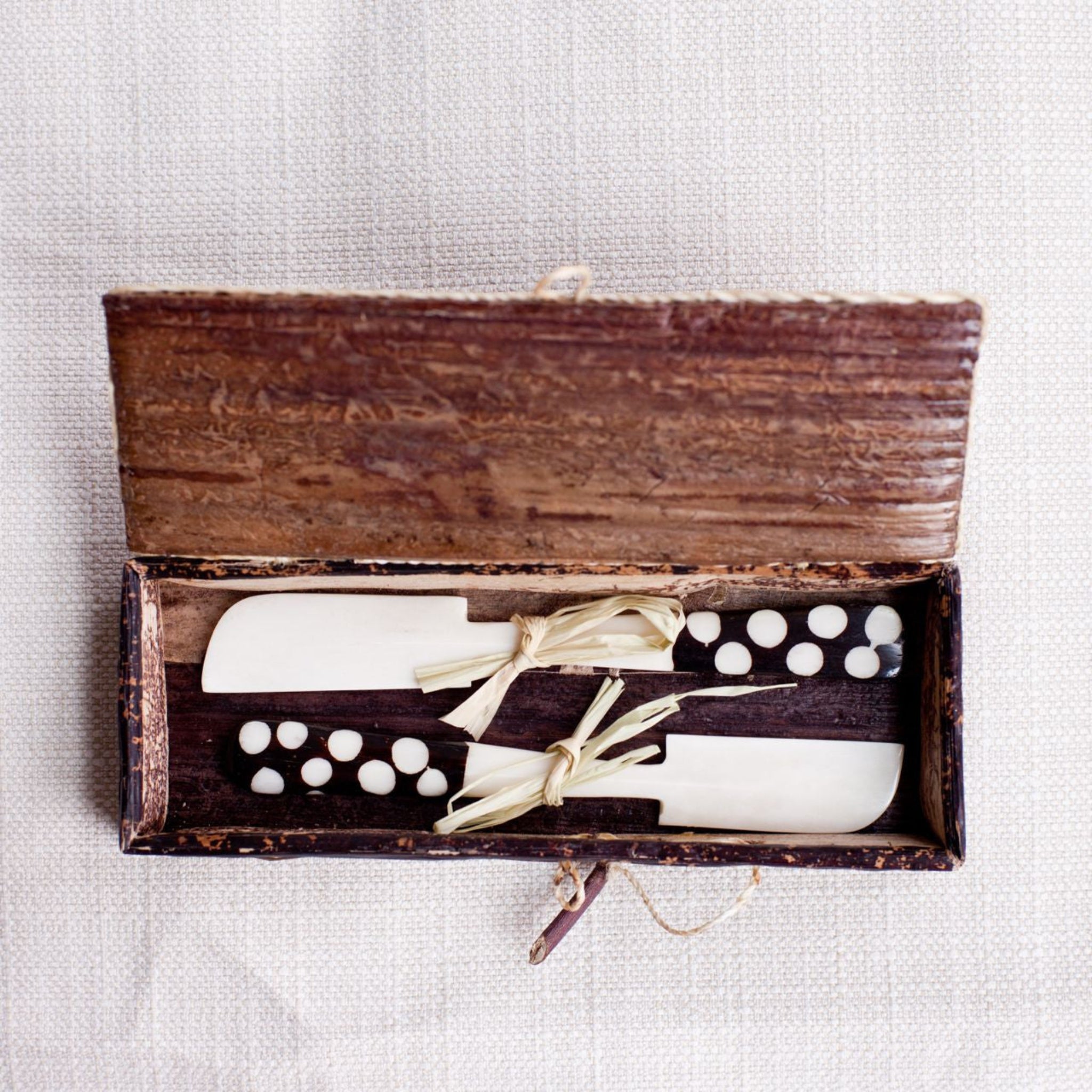 Two hand-carved cow bone knives tied with a string, displayed in an open banana leaf box.